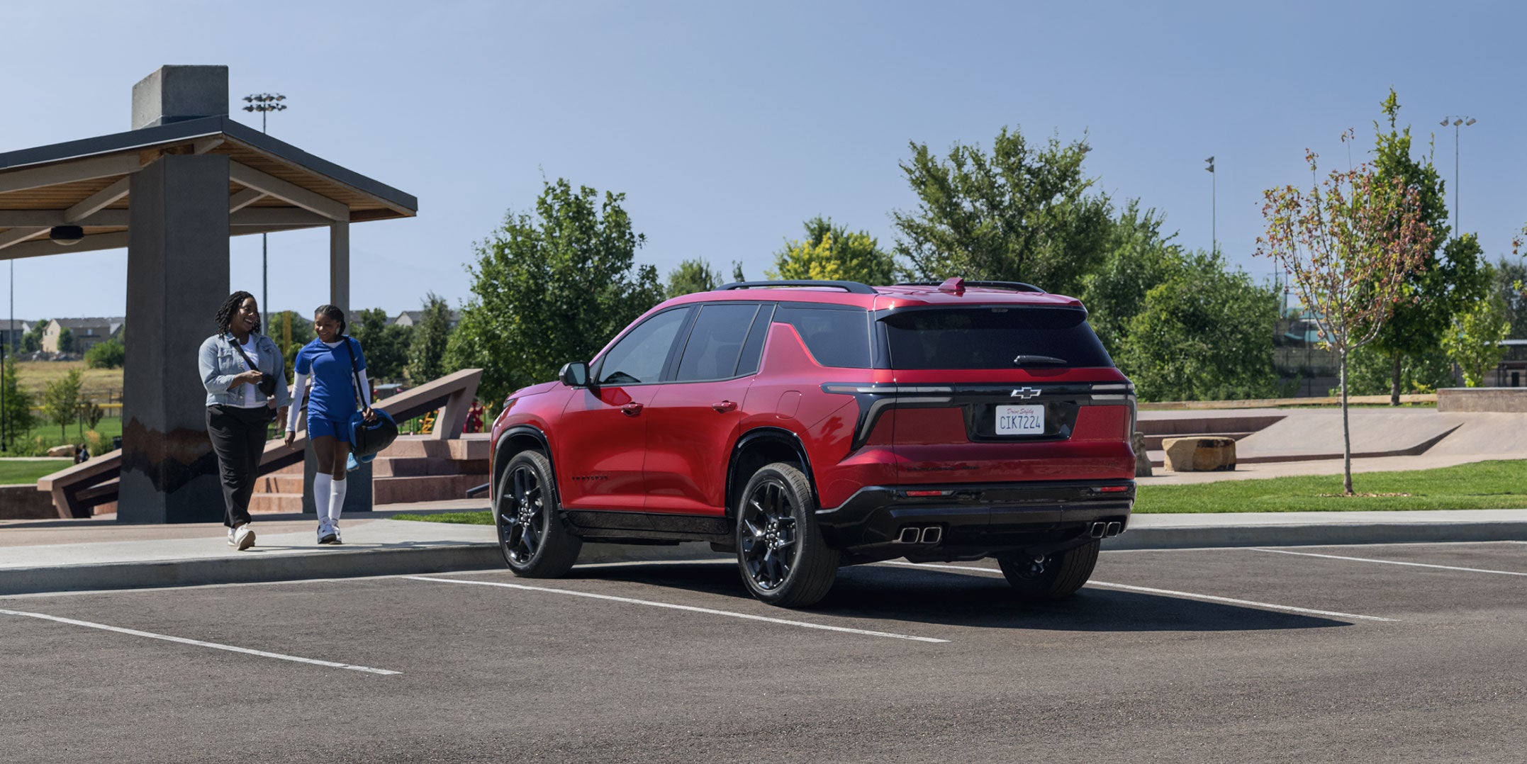 Photo of two people walking towards a red 2024 Chevrolet Traverse vehicle